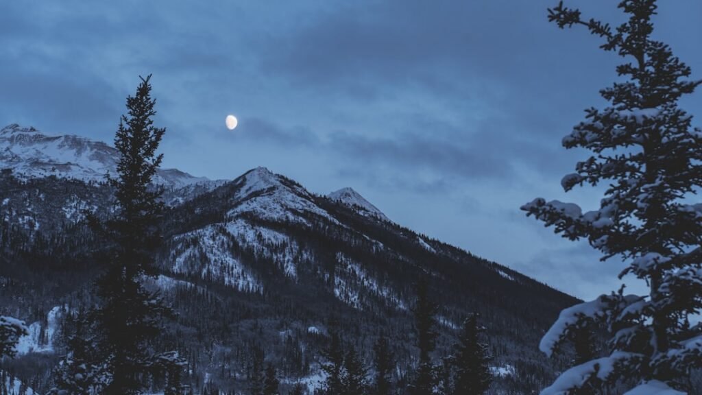 Full moon rising over a snowy mountain range, illustrating Snow Moon meaning and ritual in February
