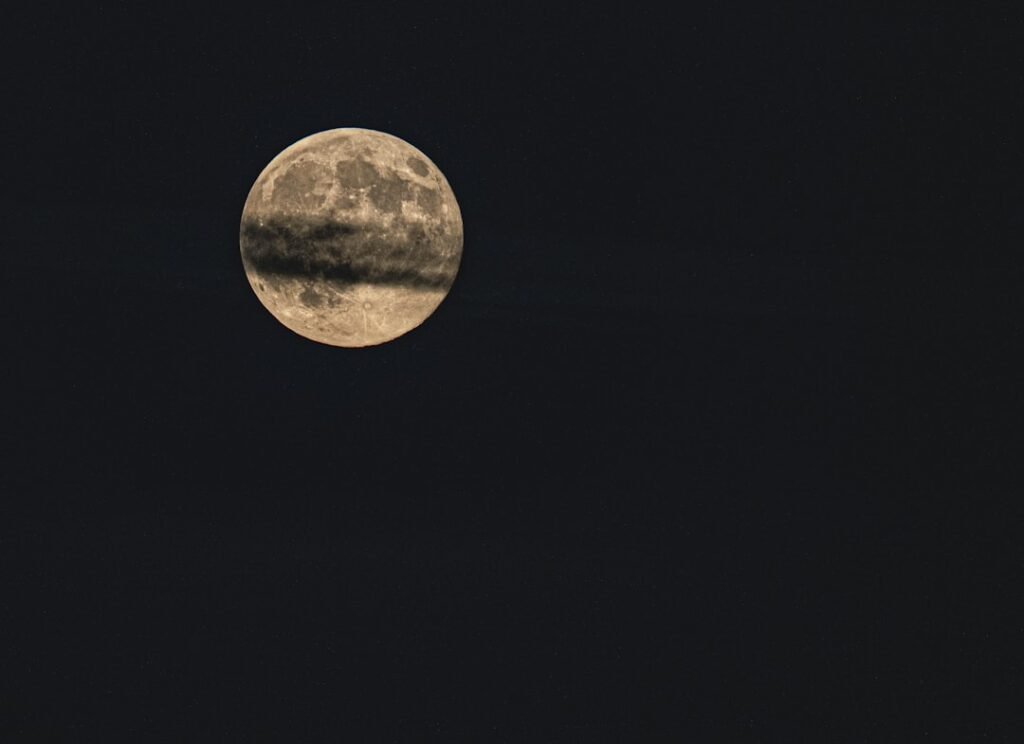 Full moon partially obscured by dark clouds, evoking sound healing frequencies and night listening practice